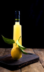 Lemoncello in a bottle on a black background, Traditional Italian liqueur from lemons. Alcohol yellow and fresh lemon with green leaves. Place for text.