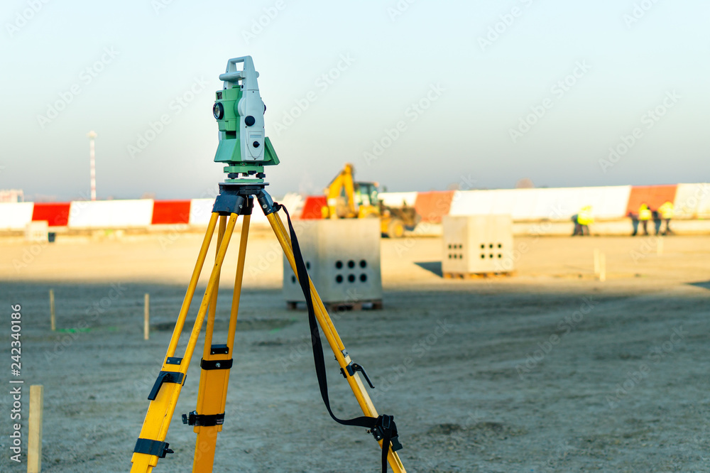 Wall mural Surveyor equipment (theodolite) on construction site of the airport, building or road with construction machines in background