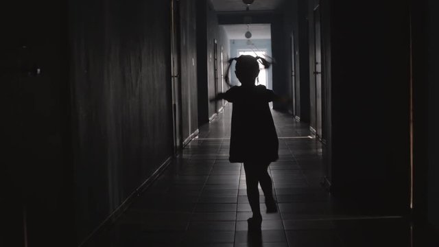 Rear view of silhouette of playful little girl wearing dress jumping the rope along hallway