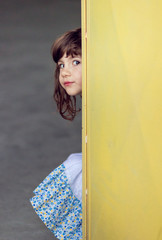 Adorable, cute, little girl peeking behind yellow wall