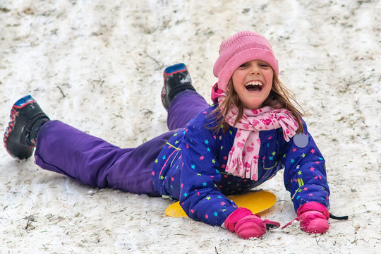 The little girl goes down the snow on the stomach
