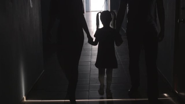 Tilt up of silhouettes of little daughter holding hands with mother and father and walking with balloon along hallway