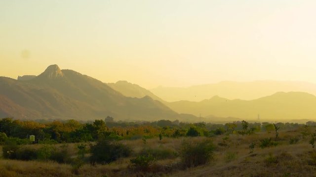 Panning shot of the Aravali mountain range in rajasthan at dusk with fog. The rocky mountains in the distance and the arid desert landscape showcase the climate of Rajasthan. The aravalis can be seen