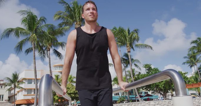 Fitness man training working out muscles at outdoor gym on South Beach doing parallel bars dips, Calisthenic Park South Beach, Miami, Florida