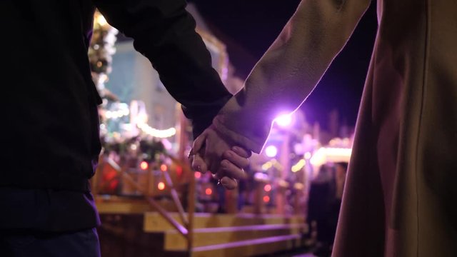 Couple in love walking holding hands on bright background of amusement park lights