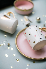 White set with a pink plate and mugs with hearts surrounded by gold sparkles. Festive Christmas layout.