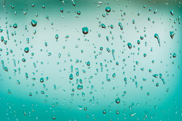 Rain drops on the window, blurred turquoise pool water in the background
