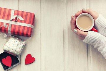 Love concept. Female hands holding a cup of coffee, red heart in a box on a wooden table. Top view.