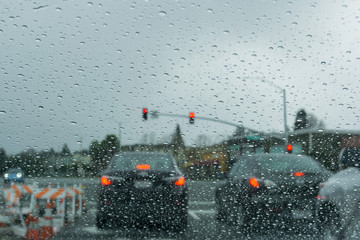 Raindrops on the windshield on a rainy day, traffic light background, California