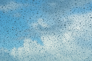 Raindrops on the windshield; in the background blue sky and white clouds, California