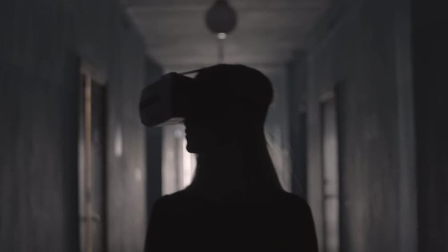 Silhouette of woman wearing VR headset and looking around while walking along hallway