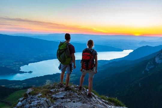 Hikers enjoying scenic view of valley with lake at sunset, couple enjoying summer outdoor trek in mountains, active lifestyle, two people backpacking