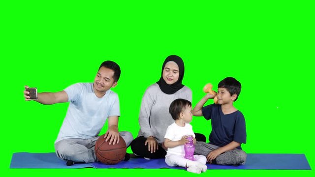 Happy young family taking selfie photo together while sitting on the mattress after exercising. Shot in 4k resolution with green screen background