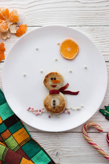 Snowman made from cheesecakes and fruits on a wooden white table , breakfast or lunch for children, creative food serving, food art - holidays, celebration and children concept