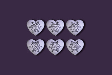 White hearts with glitter silver snowfalakes pattern on a purple background. Saint Valentine's Day concept. Flat lay. Top view.