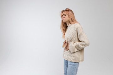 Portrait of cute woman in white sweater suffering from stomach ache, having menstruation pain, feels bad, abdominal cramps, side view. Menstrual period, gynecology, gastritis, healthcare concept.