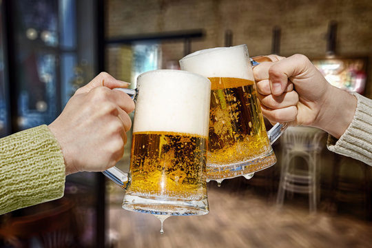 Two hands are clinking beer mugs.