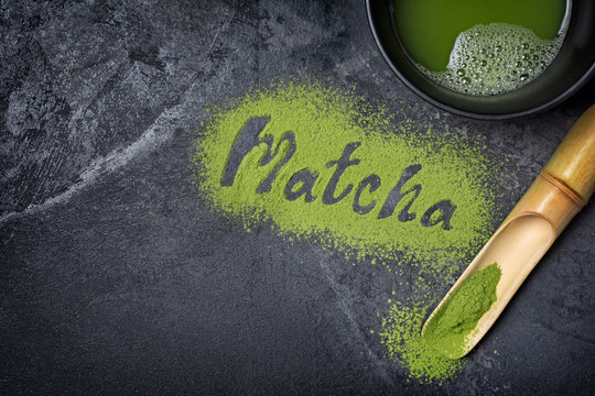 Fototapeta Lettering from green matcha tea with bamboo scoop on black marble background