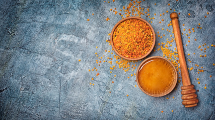 Top view on natural products honey and bee pollen in wooden bowls with honey stick