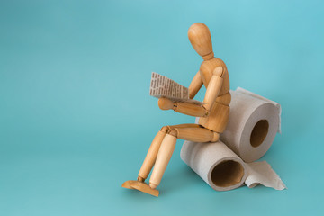 Wooden figure sit on a roll of toilet paper and reading the newspaper