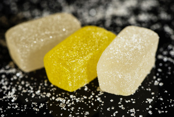 Multicolored jelly candies are sprinkled with sugar on a black background.