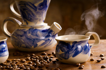 Alternative coffee brewing method, using pour over dripper and paper filter.. Two cups of coffee and a coffee pot on a wooden table. Coffee beans on a table. 