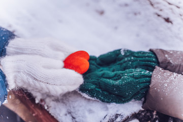Hands in gloves holding heart closeup on winter snow background. Toned.