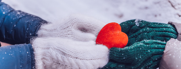 Hands in gloves holding heart closeup on winter snow background. Toned.