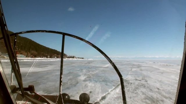 View from of moving airboat air glider on ice on background of winter landscape with mountain coast and clear blue sky of Lake Baikal in Siberia.
