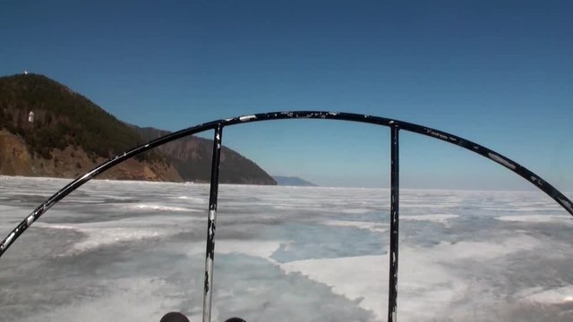 View from of moving airboat air glider on ice on background of winter landscape with mountain coast and clear blue sky of Lake Baikal in Siberia.