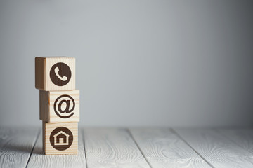 Symbols of contacts (phone, email and address) on wooden cubes on neutral background
