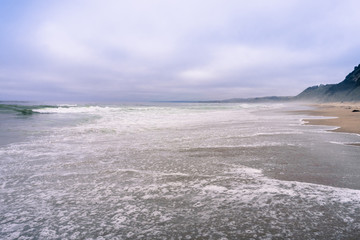 Water covering a sandy beach on the Pacific Ocean coastline on a foggy afternoon, California