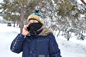 Fototapeta na wymiar talking on the phone boy in a knitted hat with a bubo and balaclava on a winter walk