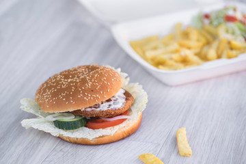 tasty delicious hamburger in box with French fries and vegetable, grey background, wood pattern, light picture, close up of meal, unhealthy fast food option for eating