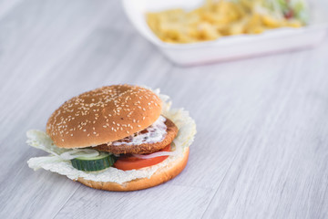 tasty delicious hamburger in box with French fries and vegetable, grey background, wood pattern, light picture, close up of meal, unhealthy fast food option for eating