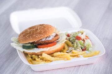 tasty delicious hamburger in box with French fries and vegetable, grey background, wood pattern, light picture, close up of meal, unhealthy fast food option for eating