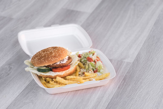 tasty delicious hamburger in box with French fries and vegetable, grey background, wood pattern, light picture, close up of meal, unhealthy fast food option for eating