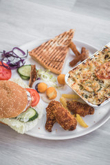 mix of fast food dishes served on plate on white wood table, unhealthy option of eating