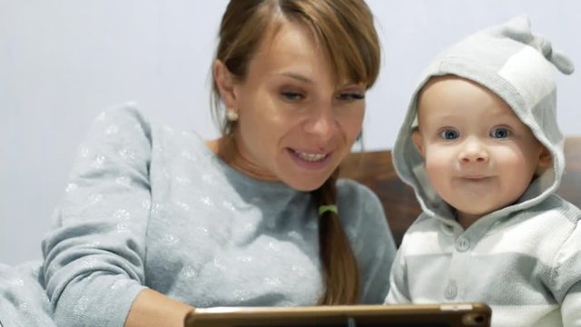 Mother and her little son watch a video. They are surprised by what they see and look into the camera. Early child development concept