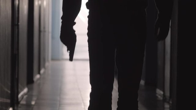 Tilt up shot of silhouette of unrecognizable man walking with handgun along dark hallway
