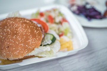 tasty delicious hamburger in box with French fries and vegetable, grey background, wood pattern, light picture, close up of meal, unhealthy fast food option for eating