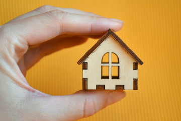 Wooden toy house model in woman's hand on yellow background front view