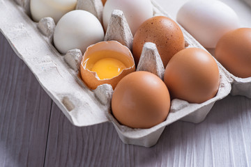 Chicken eggs and egg yolk in carton box on wooden table.