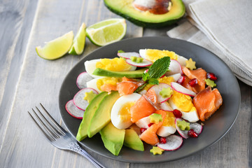 Salad with organic avocado and with salmon, eggs and radish. Decorated with mint leaf and pomegranate. Healthy lunch, vegetarian food, diet dish. food for weight loss. Selective focus and copy space