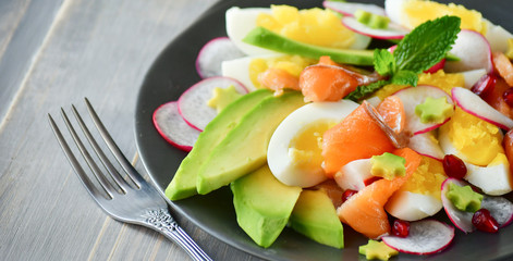 Salad with organic avocado and with salmon, eggs and radish. Decorated with mint leaf and pomegranate. Healthy lunch, vegetarian food, diet dish. food for weight loss. Selective focus and copy space