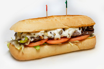 Philadelphia Cheesesteak sandwich on a sub bun with tomato and lettuce.  Tooth picks.  Isolated on white background.