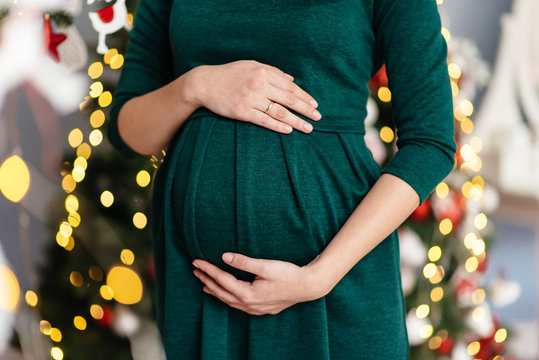 Pregnant has his hands on his stomach on the background of Christmas lights