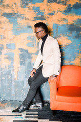 Profile side view portrait of cheerful optimistic positive handsome african american man in suit isolated over bright background sitting in orange armchair