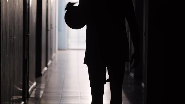 Rear view of silhouette of male basketball player in sportswear walking along hallway and dribbling the ball 