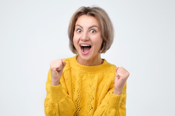 Happy caucasian woman raising fists in winning gesture and celebrating success.